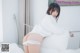 A woman in a white shirt and panties sitting on a bed.
