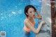 A woman in an orange bathing suit leaning on the edge of a swimming pool.